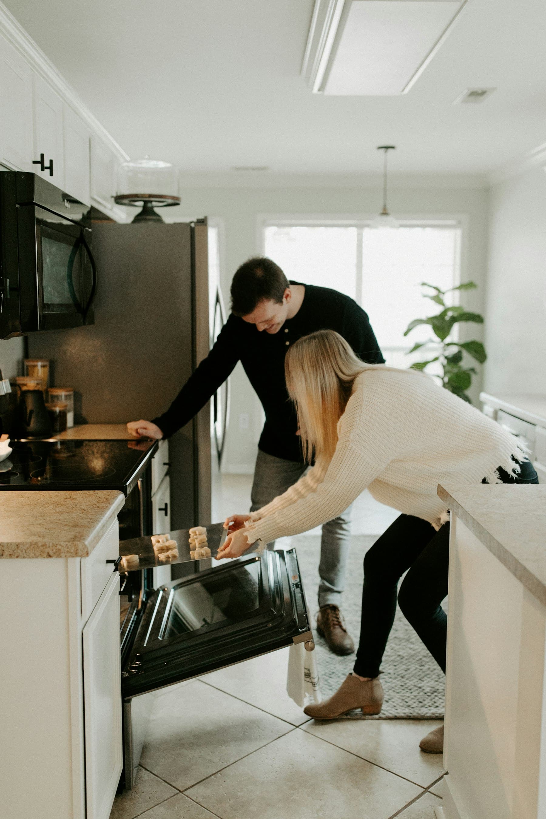 A couple pulling biscuits from the oven together.